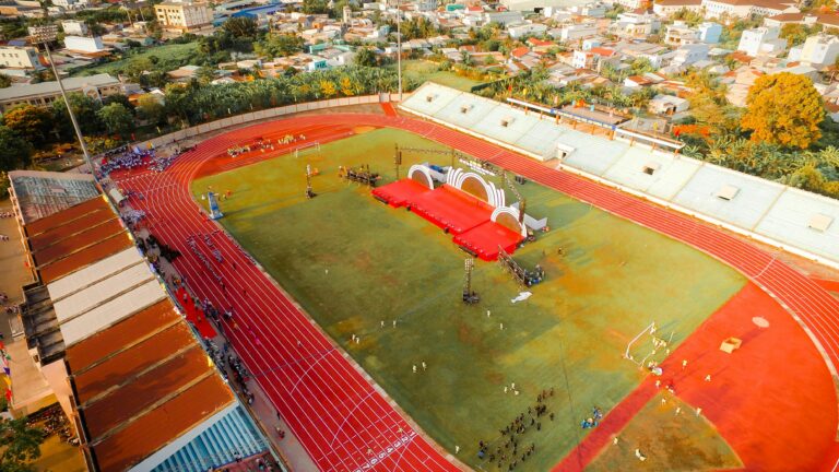 Aerial view of a lively urban stadium with a track field and stage setup, colorful and active.